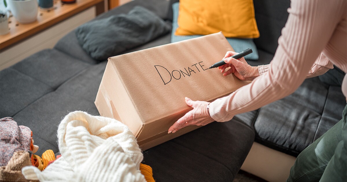 A person marks a cardboard box with the word "donate". They are preparing for a long distance move.