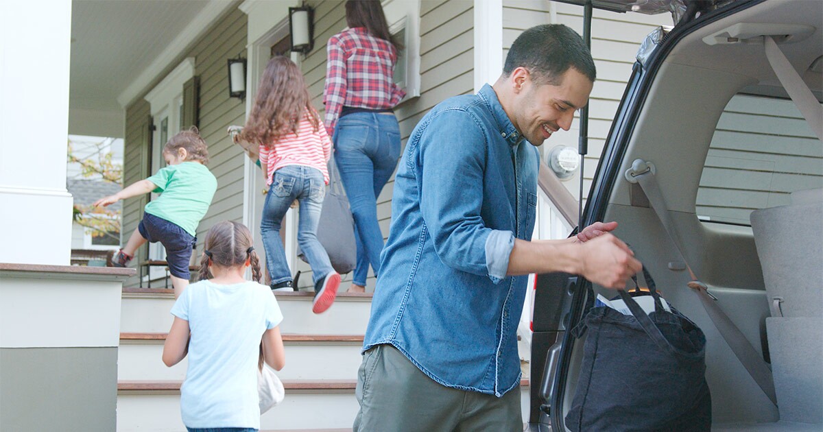 A family of five unloads a car and heads into their new home after a long distance move. They are waiting for their moving crew to show up for their delivery window.