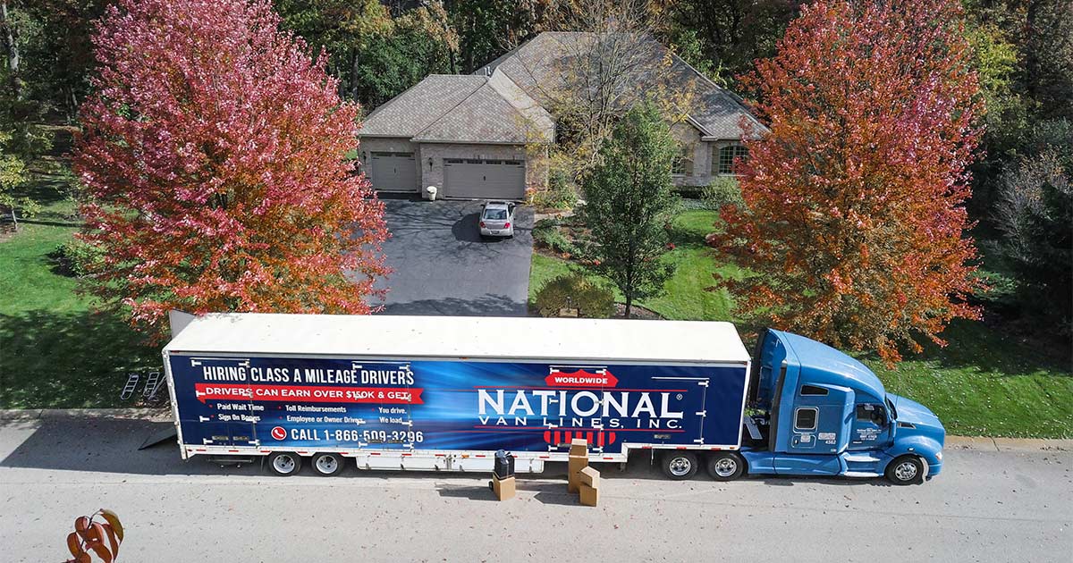 A National Van Lines truck sits parked outside a home, with moving boxes in view.