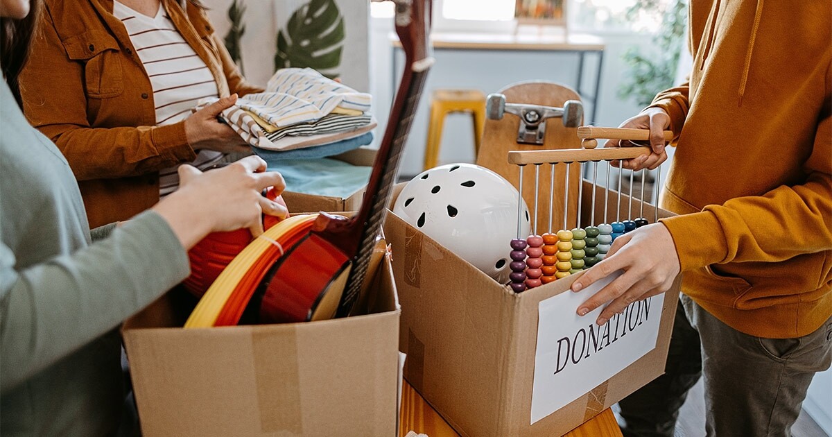 Three people sort items and clothes into boxes marked for "donation" before a long distance move.