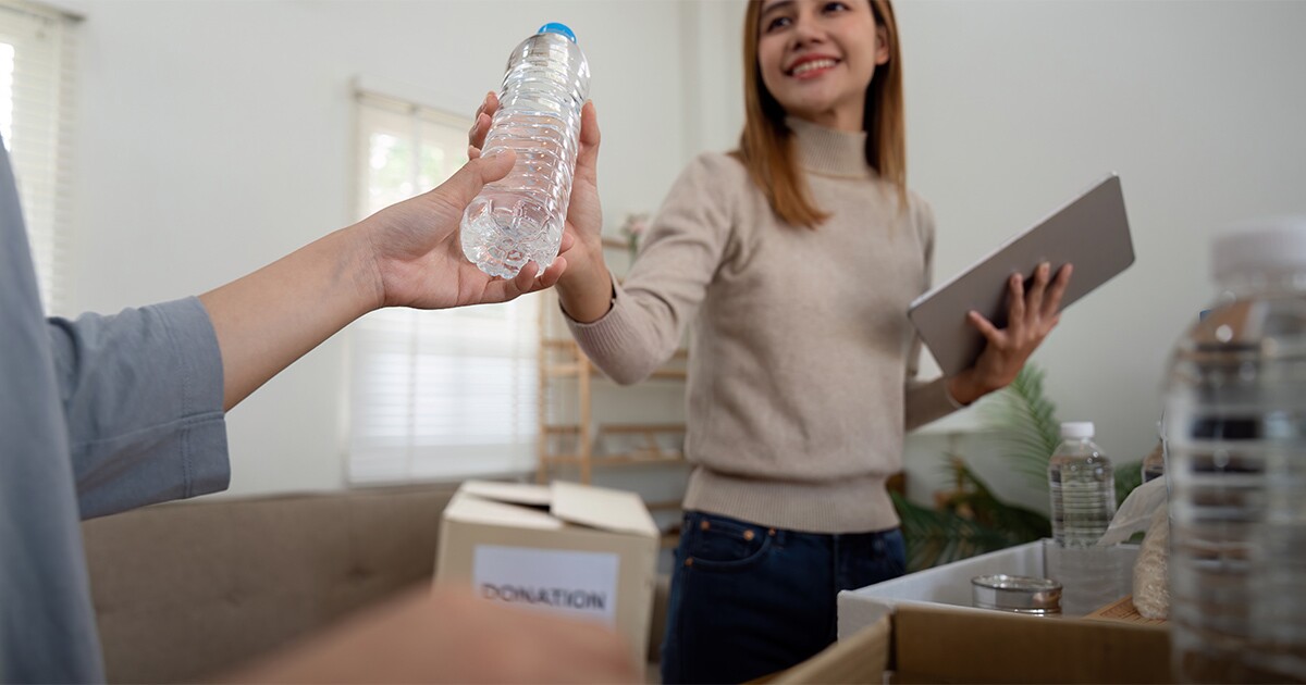 A woman hands someone in her moving crew a bottle of water. She holds a table with a moving checklist on it. She is showing her appreciation to the crew for their part in her long distance move.