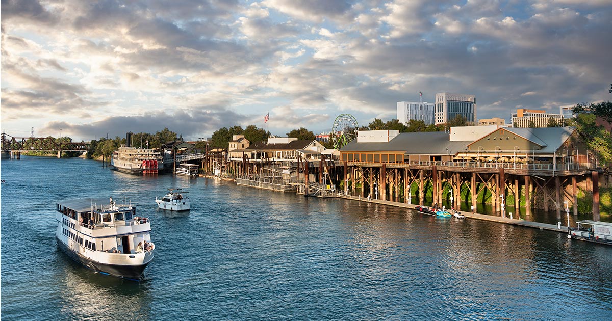 Boats sail on the river along the retail business tourist area of the old town Sacramento, CA waterfront.
