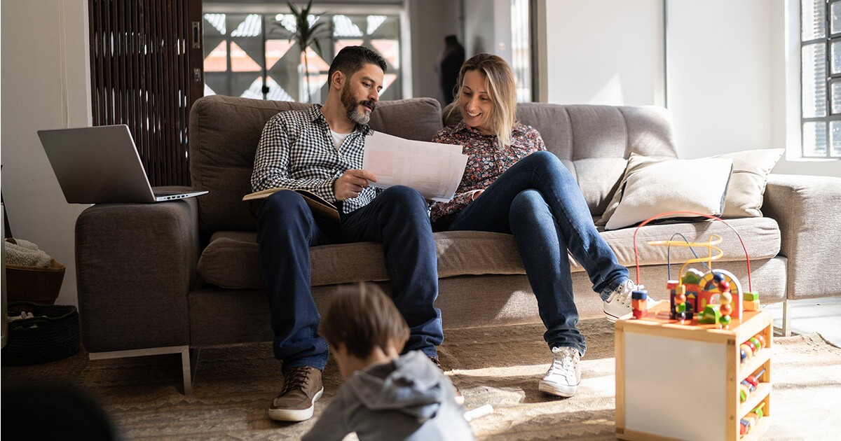 A couple sits on a couch and begins to plan their long distance move. Their child plays in the foreground. They are looking at the timeline for their upcoming move and wondering how far in advance they should book a mover. 