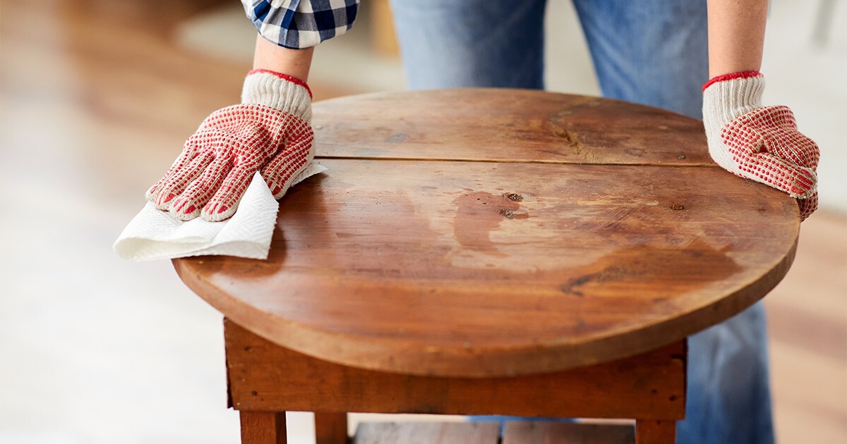 Someone wearing work gloves wipes down an antique table. It is being prepared to move cross country. 