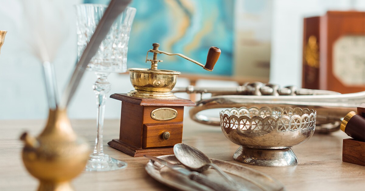 Multiple antique objects sit on top of a wooden table, including a crystal glass and a coffee grinder. These items will be prepared for a cross country move. 